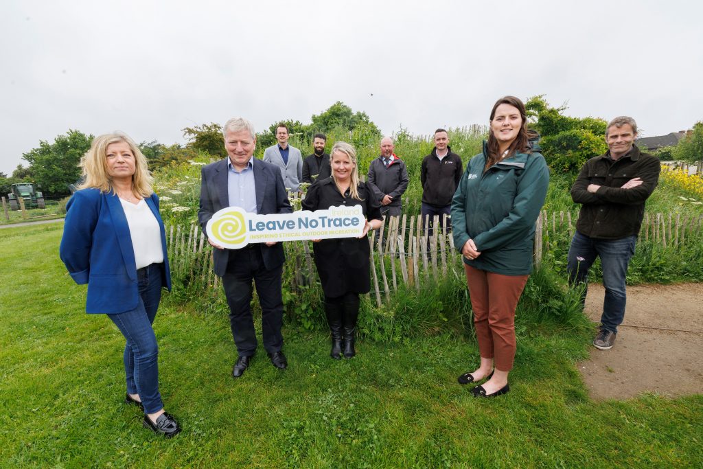 nine people standing on a grassy bank with the central two holding a leave no trace ireland banner