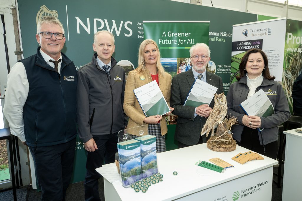 Andy Bleasdale, Mark Carlin, Ministers Pippa Hackett and Malcolm Noonan and Imelda Hurley holding a document standing behind a table and in front of an NPWS and Coillte banner